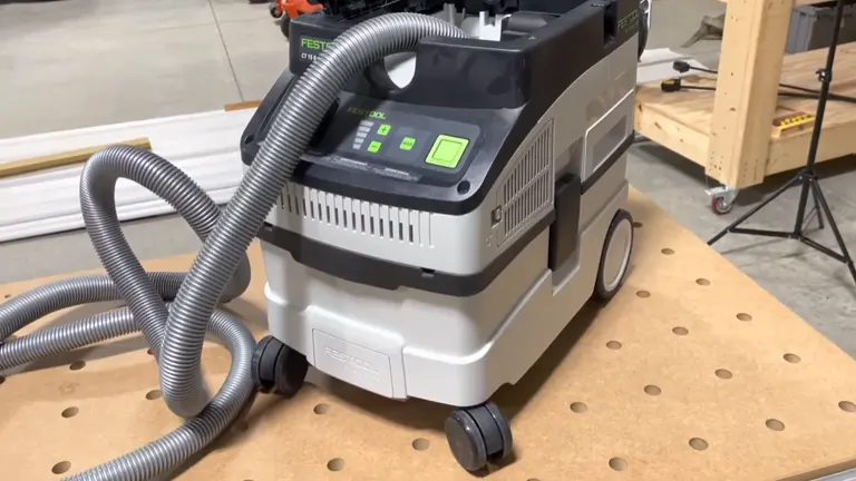 A Festool CT 15 E Dust Extractor on a wooden workbench, displayed with its flexible hose coiled beside it, showcasing the green-lit control panel and its sturdy gray body.