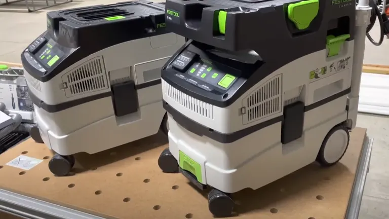 Two Festool CT 15 E Dust Extractors side by side on a wooden surface, each featuring a gray and white body with green highlights on the control panels and handles.