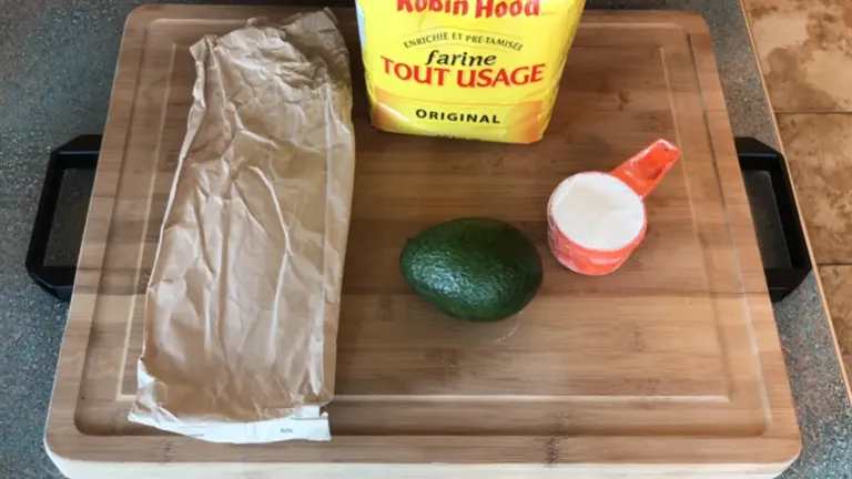 Green avocado sitting on top of a chopping board with a paper bag and flour beside it.