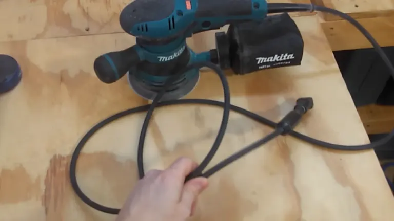 Hand holding a power cord with a Makita power tool in the background