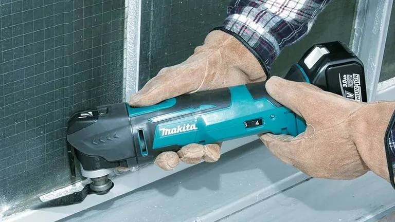 A person using the Makita oscillating multi-tool to trim metal on a window frame, wearing protective gloves.