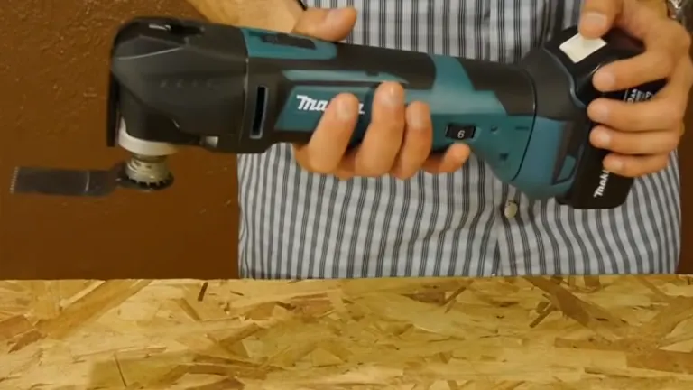 Close-up of the Makita multi-tool being used to cut through a thin piece of wood, held by a person in a striped shirt.