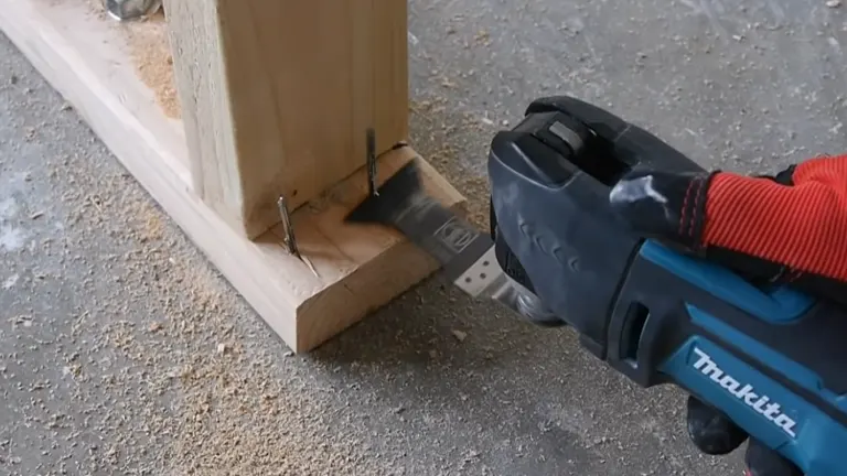 Makita oscillating multi-tool cutting through a wooden plank with nails, demonstrating its cutting capability.