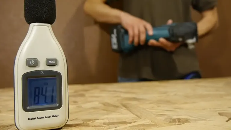 Digital sound level meter displaying a reading of 84 decibels, next to a person using the Makita multi-tool in a workshop.