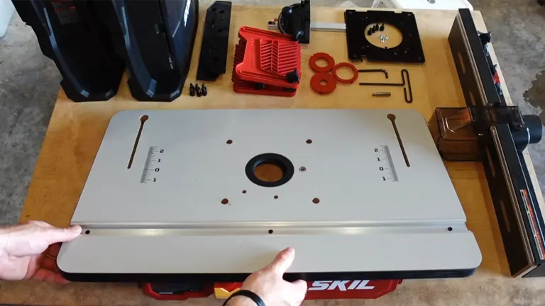 Close-up of SKIL SRT1039 Router Table showing its grey laminated top, central router hole, and various accessories laid out, including red featherboards and insert rings.