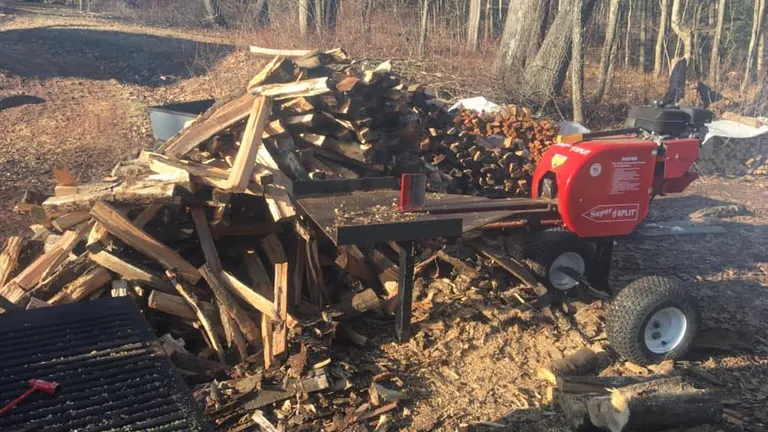 SuperSplit Log Splitter in a forest with a scattered pile of logs.