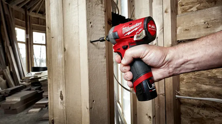 A Milwaukee hydraulic impact driver being used to drive a screw into a wooden structure, demonstrating its compact design and power.