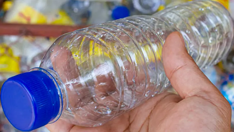 Close-up of a hand holding an empty plastic water bottle with a blue cap, preparing for recycling or reuse.
