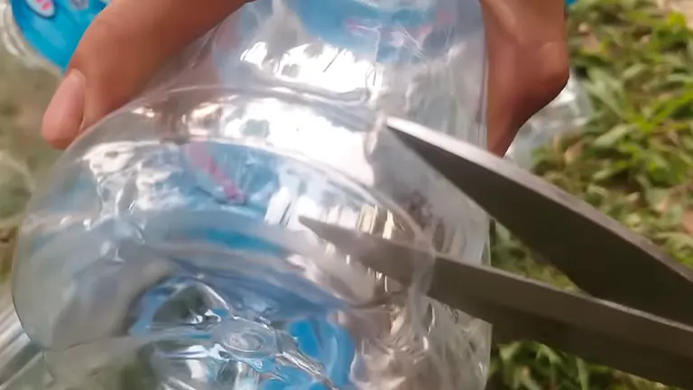 Action shot of scissors cutting the bottom off a clear plastic water bottle, preparing it for use in a drip irrigation system.
