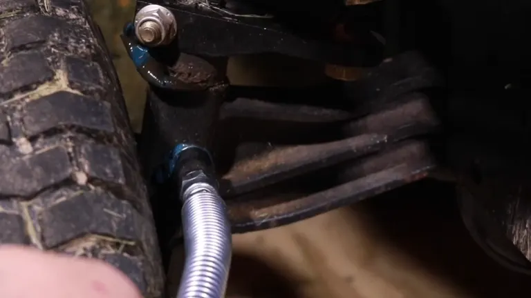 Grease gun hose attached to a vehicle part for lubrication.
