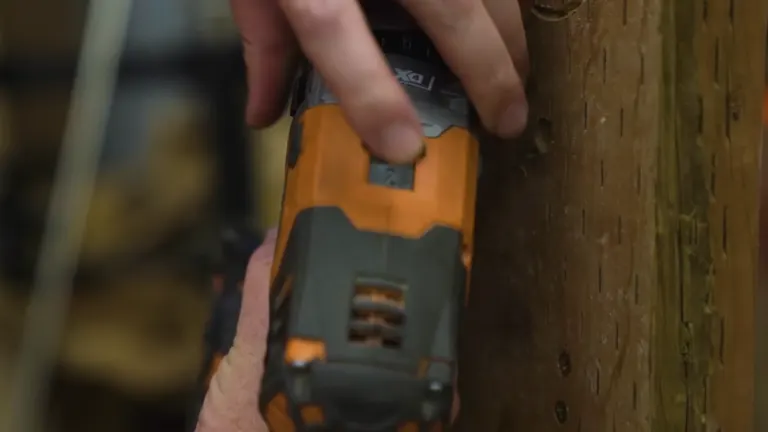 Close-up of a man’s hand adjusting the chuck of an orange cordless drill.
