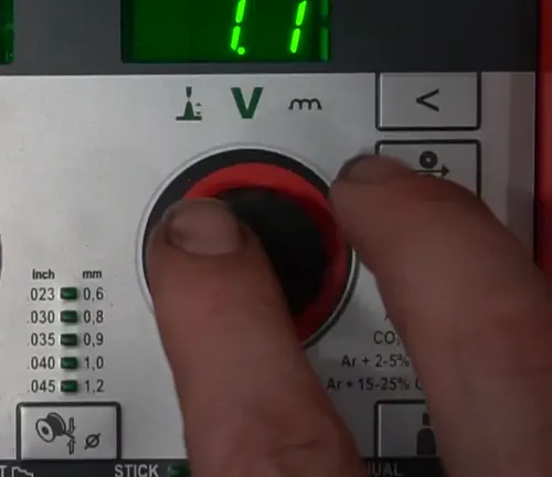 Close-up of a hand adjusting the settings on the Fronius TransSteel 2200 welder's control panel.