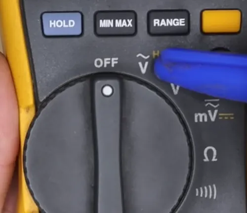 Close-up of multimeter knob with a hand adjusting settings, highlighting OFF, voltage, and resistance modes.
