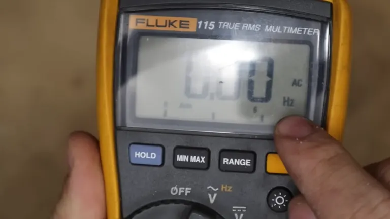 Multimeter set to measure AC voltage, displaying a reading of 0.0 with a person's thumb on the range button.