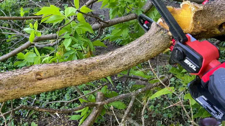 Skil Mini Chainsaw cutting through a thick branch outdoors with chips flying.
