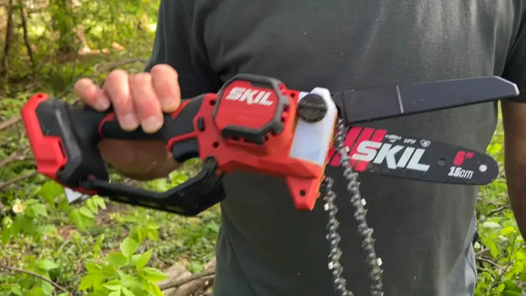 Person holding a Skil Mini Chainsaw with chain and guide bar visible.
