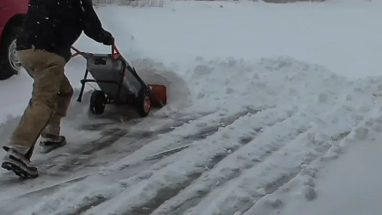 Man using a WORX Aerocart to clear snow from a residential driveway.