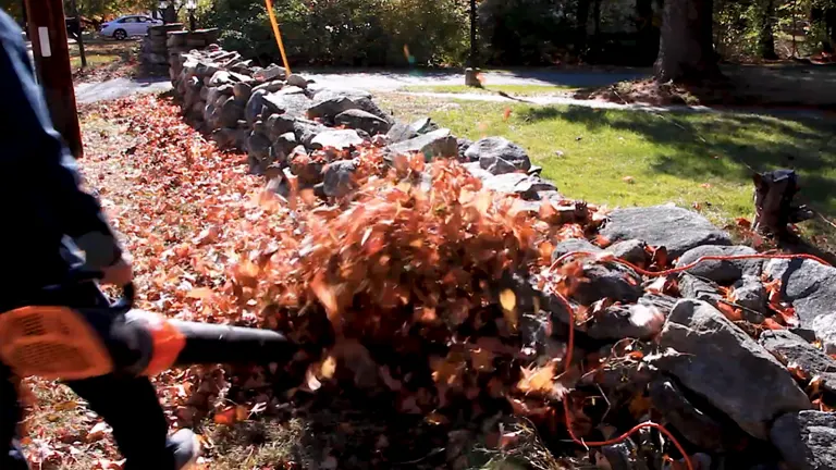 Dynamic action shot of a Worx Turbine 600 electric leaf blower expelling a large volume of leaves along a stone-bordered garden path.