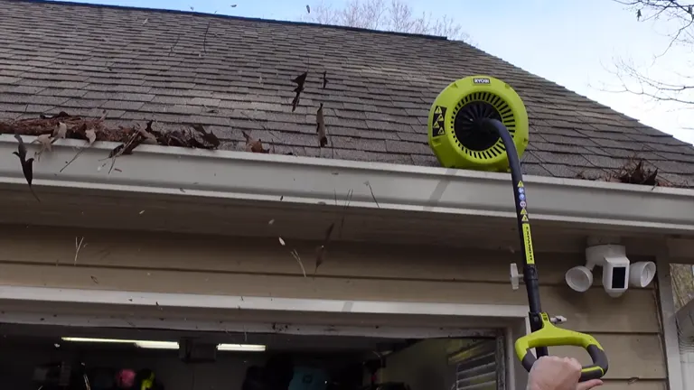 Ryobi gutter cleaner in use, discharging leaves from gutter at the end of a house.
