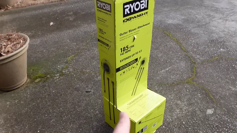 Box of Ryobi EXPAND-IT Gutter Blower Attachment lying on a driveway.
