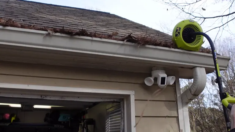 Ryobi gutter cleaner attached to a blower, clearing heavily leaf-filled gutter on a house.
