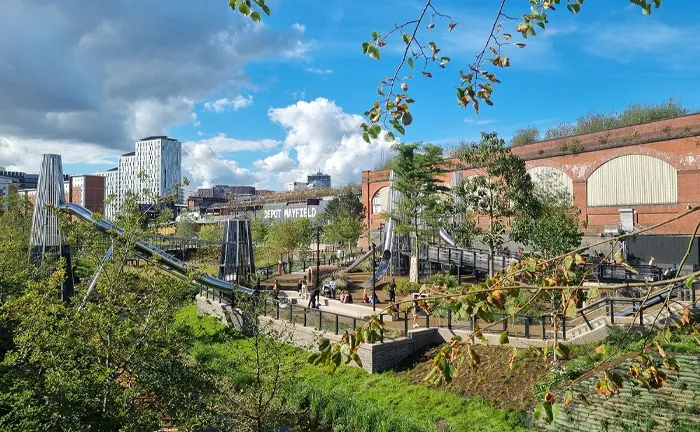 Urban park with trees, people, and modern structures under a blue sky, illustrating sustainable forest management of 5 Tips to Maximize Biodiversity in Your Sustainable Forest