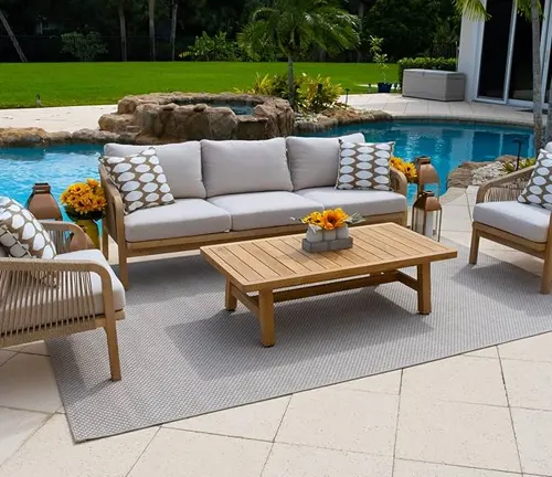 Outdoor patio furniture set near a pool, featuring a wooden table, sofa, and chairs with white cushions.