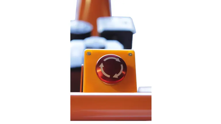 Close-up of an emergency stop button on the POWER KING wood chipper, featuring a circular red button with an arrow indicating rotation for operation.