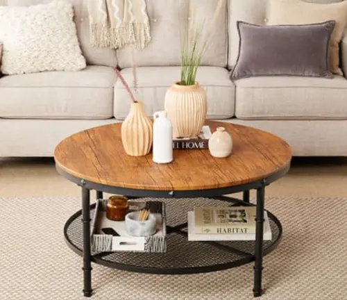 Round wooden coffee table with black metal legs, decorated with vases and a book, in a cozy living room.