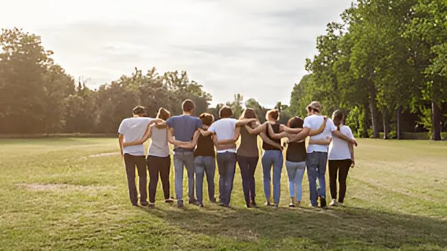 Group of people standing arm in arm in a park.