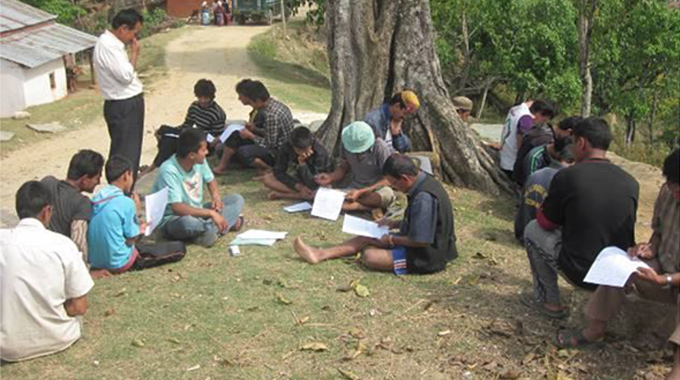 A group of people gathered outdoors under a large tree, sitting on the ground and engaged in a discussion or meeting.