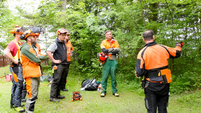 A forestry instructor briefing a group of trainees in safety gear before fieldwork.