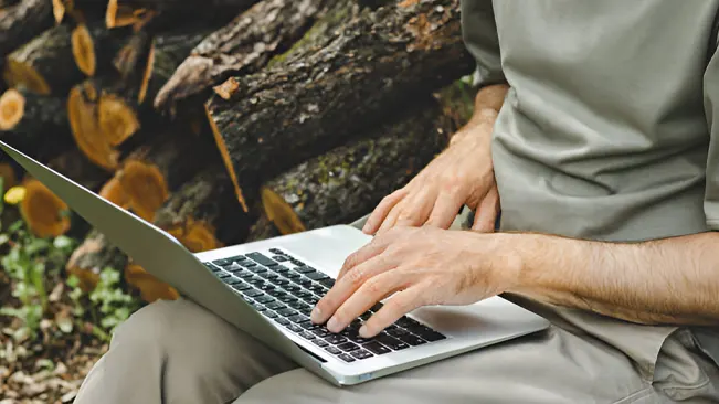 Person using a laptop in the forest, studying online courses and workshops.