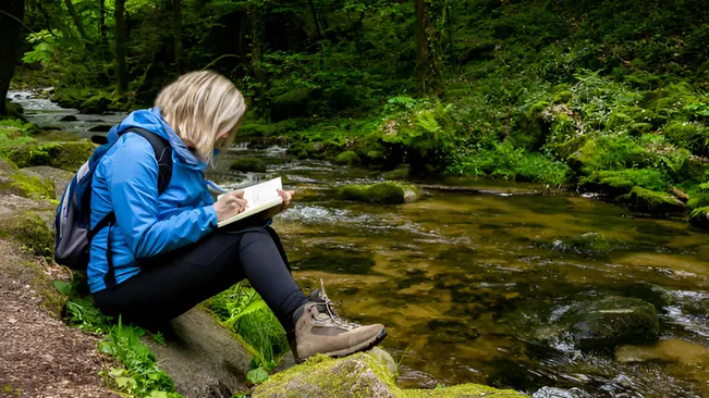 Person studying by a river in a forest, preparing for certification exams.