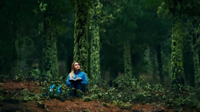 A young forester sits in a dense, moss-covered forest, holding a book and contemplating essential skills for aspiring foresters