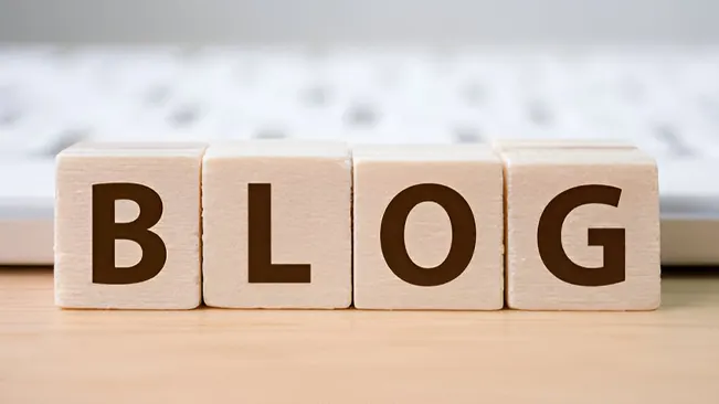Blocks spelling 'BLOG' on a wooden surface with a keyboard background, representing educational blogs.