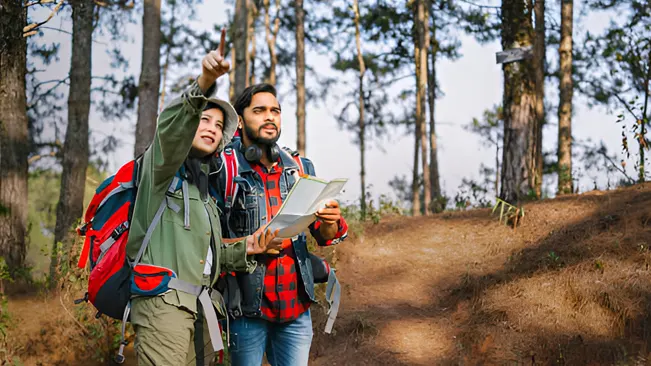 Two people in a forest with a map and GPS, illustrating monitoring and evaluating conservation efforts.