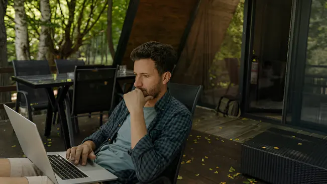 A man sitting outdoors using a laptop to find forestry jobs online.