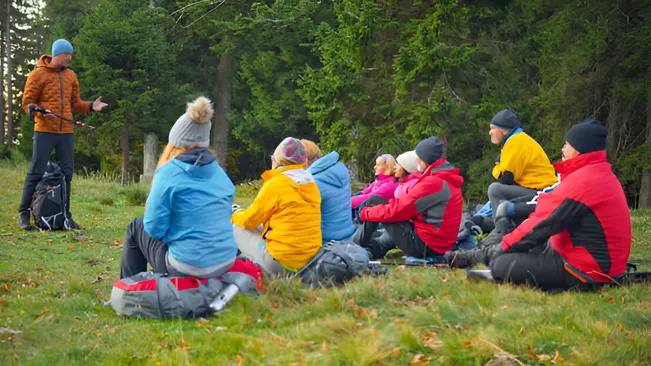 A group of people in outdoor gear sitting in a field, engaging in a community involvement activity.