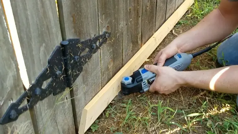 Dremel tool being used to trim a wooden fence outdoors.