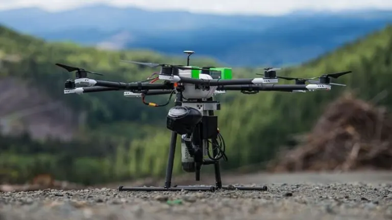 Forestry drone stationed on a rocky terrain with forested mountains in the background.
