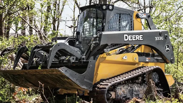 John Deere 333G compact track loader moving debris in a forested area.
