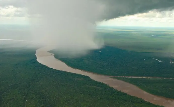 Aerial view of a rainforest with a river and a rainstorm, illustrating the role of biodiversity in climate regulation