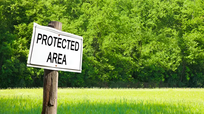 Sign reading "Protected Area" in front of a lush green forest, indicating habitat conservation.






