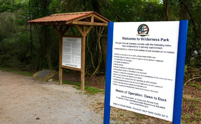 Entrance of Wilderness Park with an informational sign listing park rules and hours, aimed at promoting responsible usage and pest management.