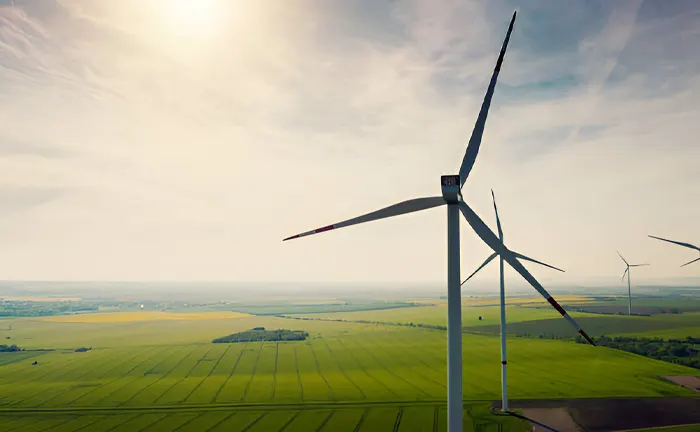 Wind turbines in a vast agricultural landscape under a sunny sky.