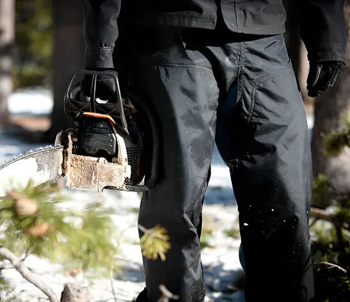 Chainsaw operator equipped with protective gear including chainsaw chaps for body protection.