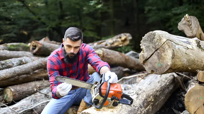 Man inspecting chainsaw for regular maintenance to ensure proper function before tree felling.