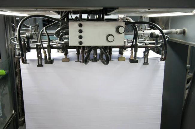  A close-up of an industrial machine gripping a stack of paper sheets, illustrating a precision stage in the production process within the pulp and paper industry.