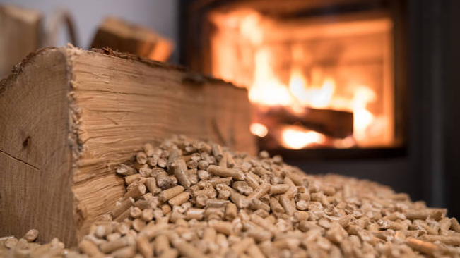 Close-up of wood pellets and a log next to a burning fire in a stove, highlighting the use of forest bioenergy as a renewable and sustainable heating source.